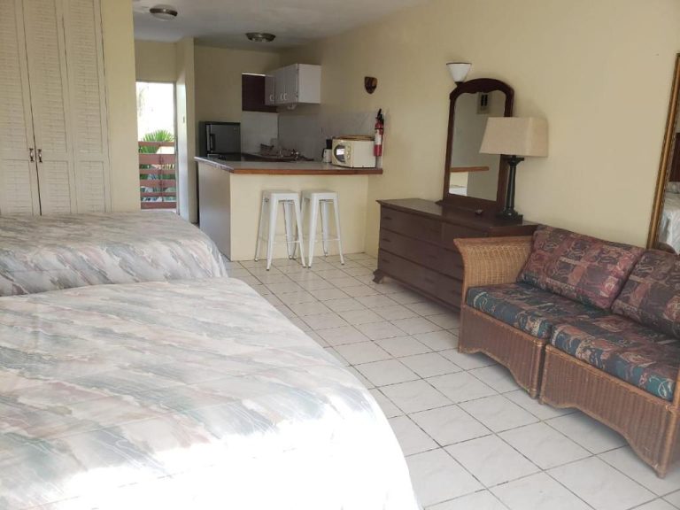 Estudio con camas dobles, cocina americana equipada y sofá de ratán en Negril Beach Club Condos