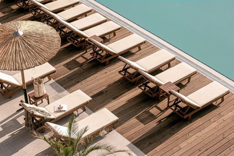 Tumbonas de madera con cojines beige junto a la piscina turquesa del Sunny Beach Club Adults Only