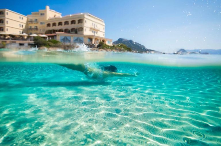 Bañista nadando en las cristalinas aguas turquesas frente al Gabbiano Azzurro Hotel & Suites en Cerdeña