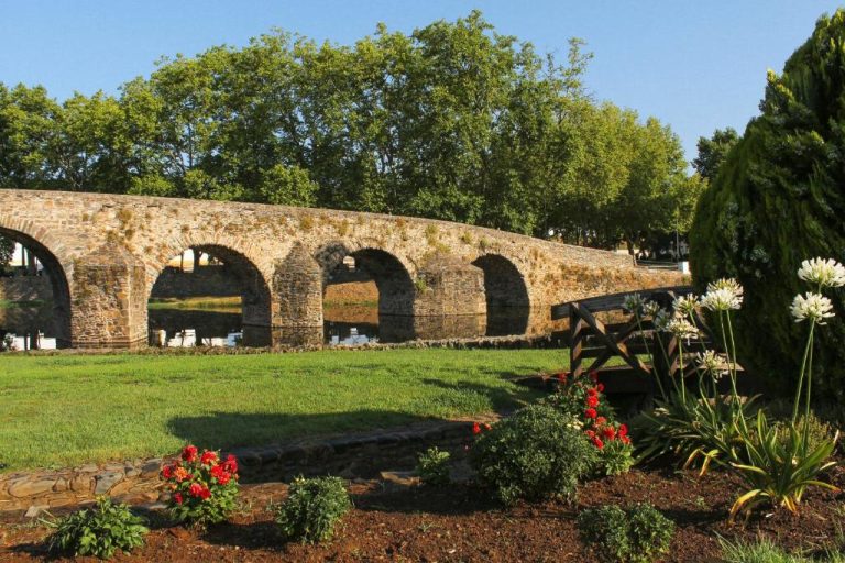 Puente romano de arcos de piedra junto al jardín con flores del Convento Da Serta Hotel