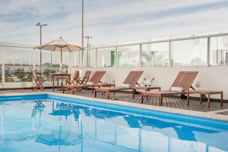 Piscina exterior con tumbonas de madera y terraza solarium del Intercity Florianopolis
