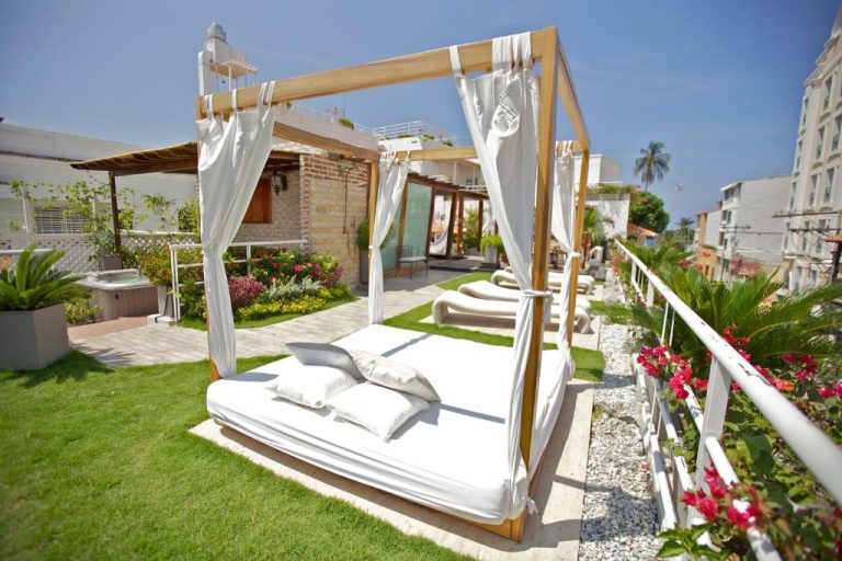 Cama balinesa con dosel blanco en la terraza jardín del Hotel Boutique Don Pepe con tumbonas y flores
