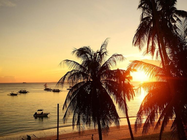 Atardecer dorado en la playa del Kaiyana Boracay Beach Resort con palmeras y barcos en el mar