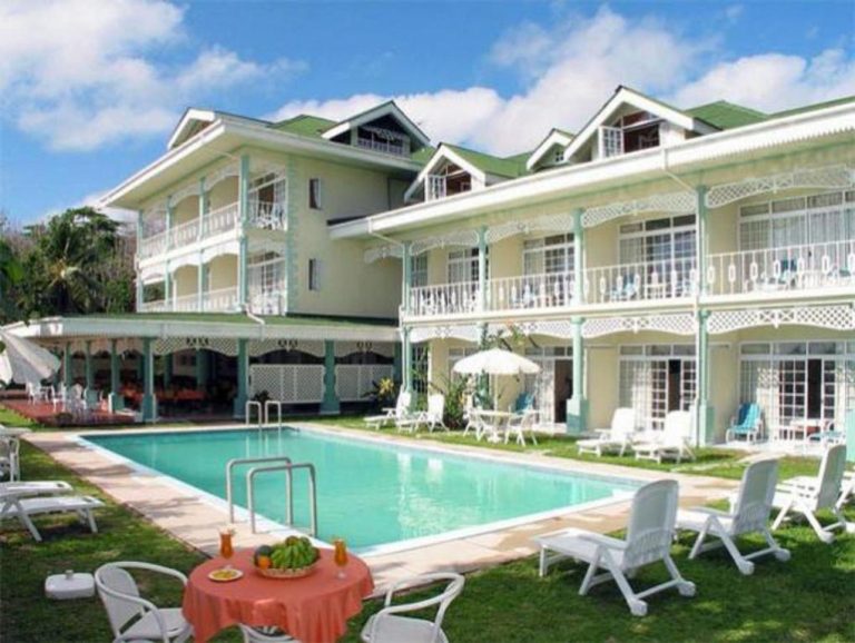 Piscina exterior con tumbonas y terraza del Palm Beach Hotel rodeada de jardines tropicales