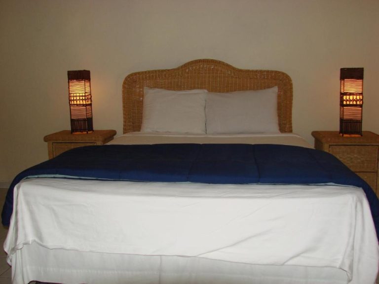 Habitación con cama doble y cabecero de mimbre en Cunucu Villas Aruba Tropical Garden Apartments