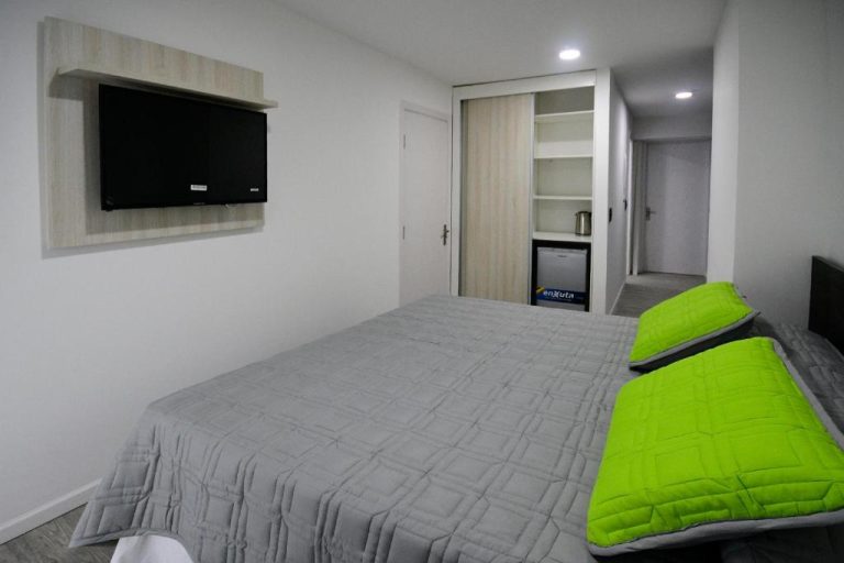 Habitación doble del Quijano Hotel con cama, TV en pared, minibar y almohadas verdes