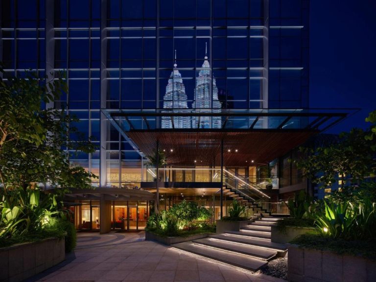 Entrada iluminada del Grand Hyatt Kuala Lumpur con las Torres Petronas al fondo durante la noche