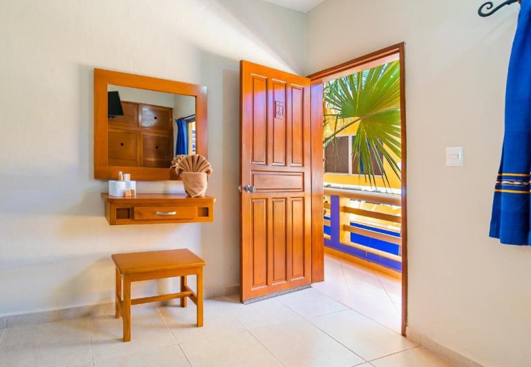 Habitación del Hotel Yumkiin con puerta de madera abierta hacia balcón con vistas a palmeras