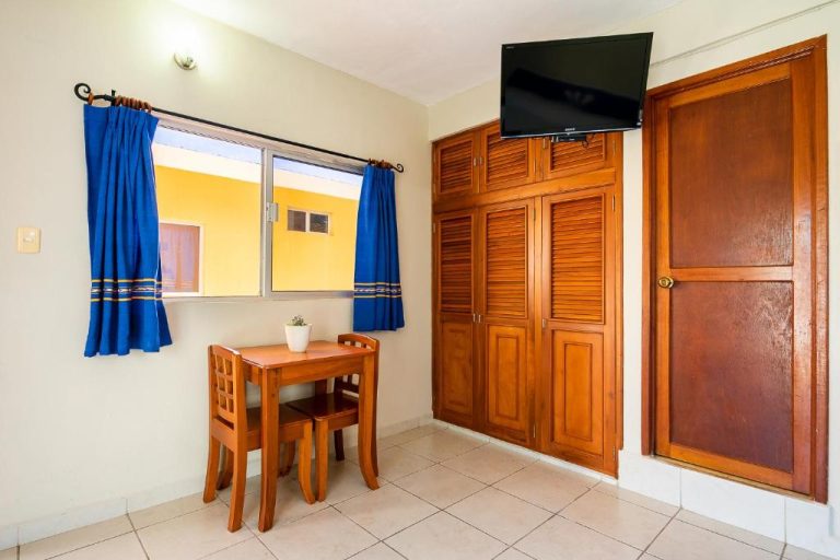 Habitación del Hotel Yumkiin con armario de madera, televisión, mesa y ventana con cortinas azules