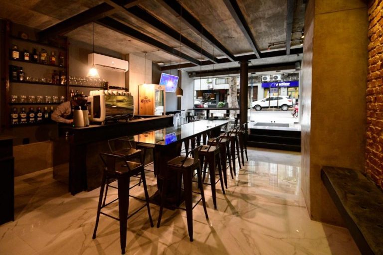 Bar lounge interior con taburetes altos y barra de madera en Quijano Hotel Aparts & Suites