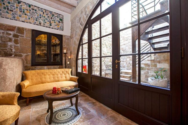 Elegante salón con arco de piedra, sofá dorado y puerta francesa en Porolithos Boutique Hotel