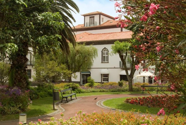 Jardín exterior con flores y bancos del Hotel Talisman, rodeado de palmeras y vegetación tropical