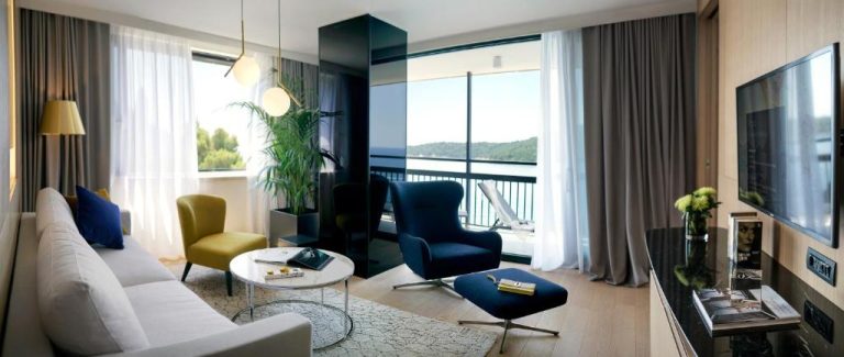 Elegante salón de suite con sofá blanco, sillones y terraza con vistas al mar en Hotel Excelsior