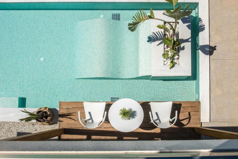 Vista aérea de la piscina turquesa con terraza de madera y mobiliario blanco en Paralos Lifestyle Beach Adults Only