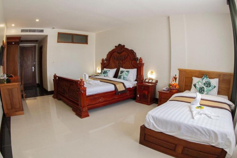 Habitación triple con camas de madera tallada y decoración tradicional en Kampong Thom Palace Hotel