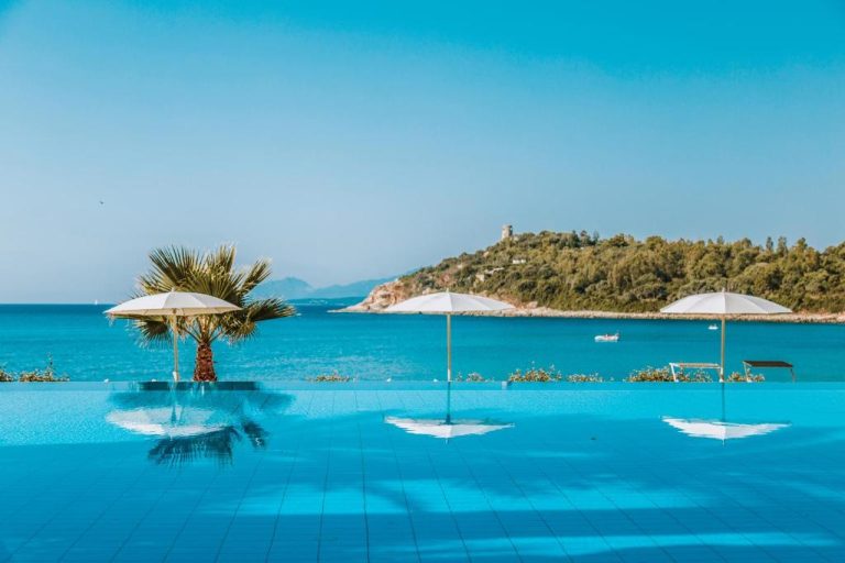 Piscina infinita con vistas al mar turquesa y palmera del Hotel La Bitta Bovis Hotels en Cerdeña
