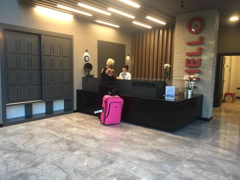 Recepción moderna del Ramira City Hotel Adult Only con mostrador negro y maleta rosa de huésped
