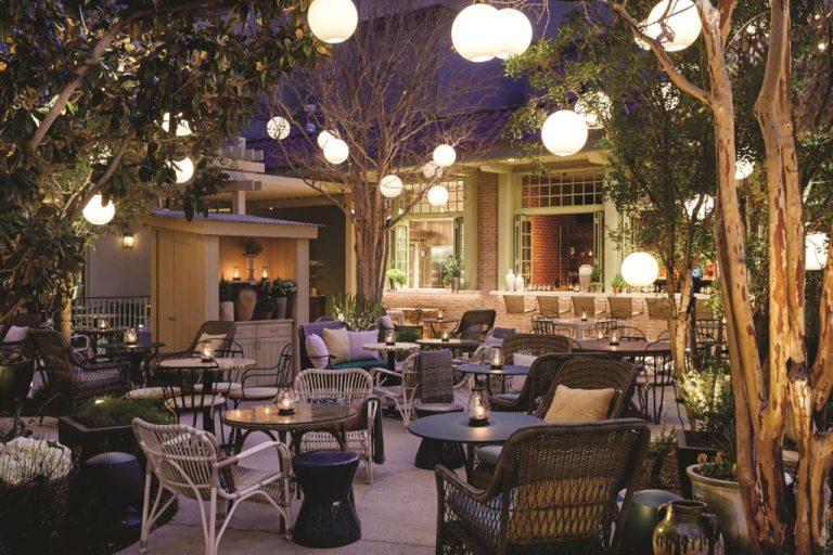 Terraza exterior iluminada con mesas y sillas de mimbre en The Reserve at Park MGM Las Vegas