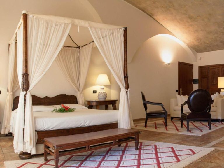 Suite con cama de dosel y techo abovedado en el Hotel Costa dei Fiori, decoración rústica elegante