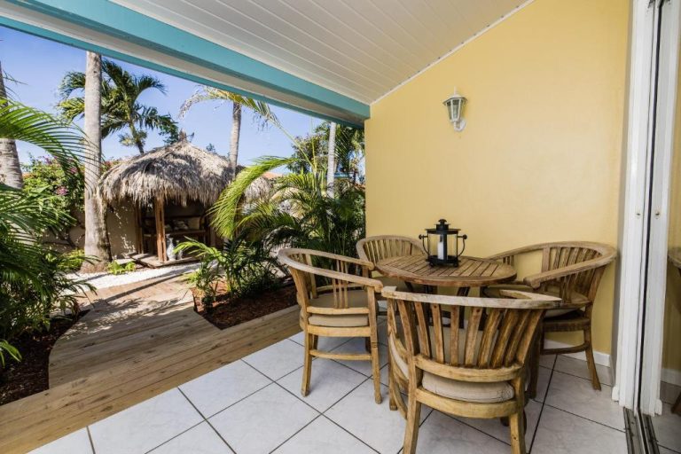 Terraza con mesa y sillas de madera en Paradera Park Aruba con jardín tropical y palapa al fondo