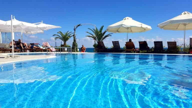 Piscina exterior con tumbonas y sombrillas blancas del Aphrodite Beach Hotel con vistas al mar