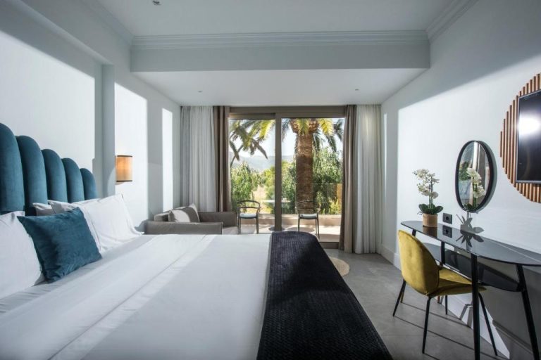 Habitación doble con cama king, cabecero azul y terraza con vistas al jardín en Drossia Palms Hotel