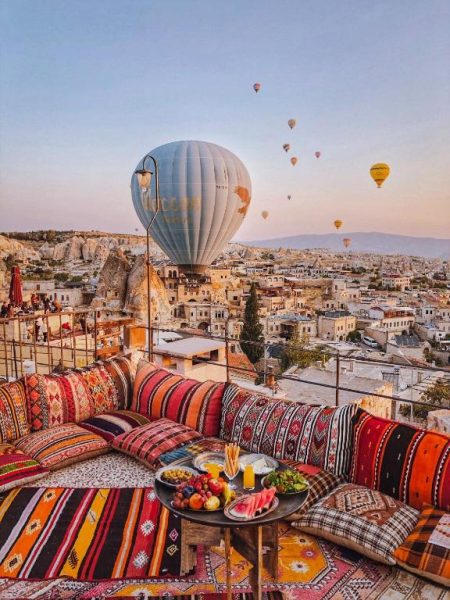 Terraza con cojines coloridos y globos aerostáticos al amanecer en Charming Cave Hotel, Capadocia