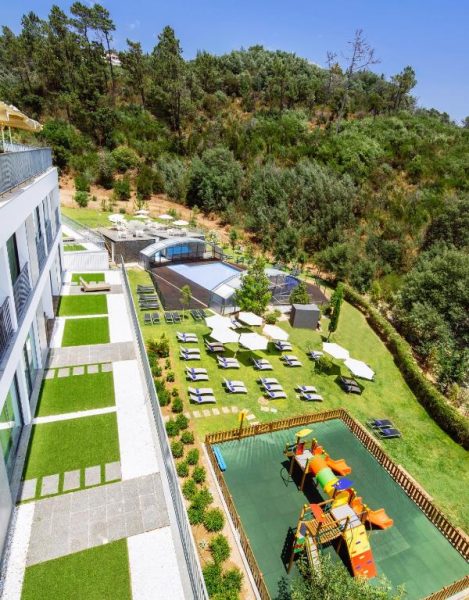 Vista aérea del jardín con piscina cubierta, tumbonas y zona de juegos infantil en Monchique Resort & Spa