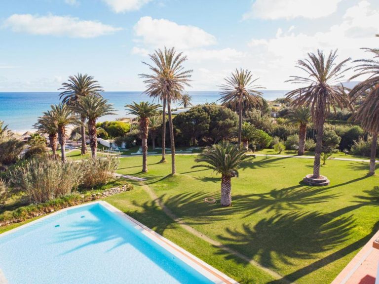 Piscina exterior con jardines de palmeras y vistas al mar del Hotel Porto Santo & Spa