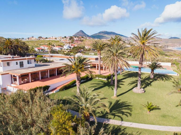 Jardines tropicales con palmeras y piscina exterior del Hotel Porto Santo & Spa en Portugal