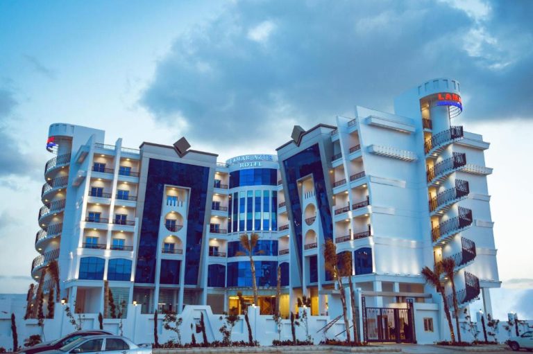 Fachada exterior iluminada del Lamar Azur Hotel con arquitectura moderna y palmeras al atardecer