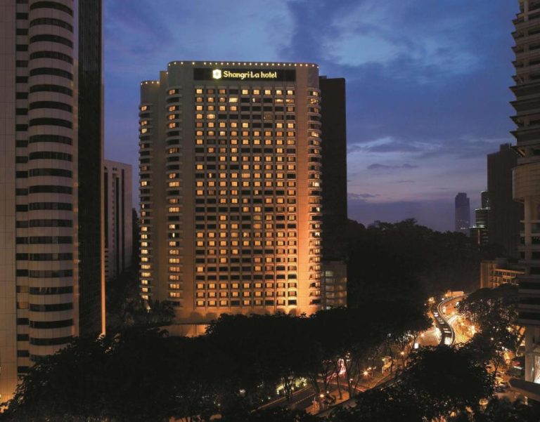 Vista nocturna de la fachada iluminada del Shangri-La Hotel Kuala Lumpur entre rascacielos