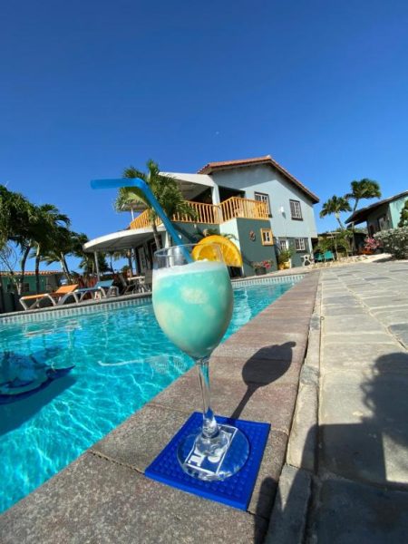 Cóctel azul tropical junto a la piscina exterior del hotel La Felicidad Aruba con vistas a la villa