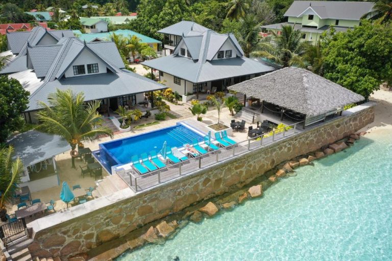 Piscina exterior con tumbonas azules del Le Nautique Waterfront Hotel La Digue frente al mar turquesa