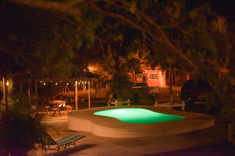 Piscina iluminada de noche con área de descanso y jardín en Hotel de Campo Villa de Ada