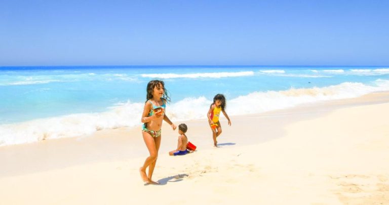 Niños jugando y corriendo en la playa de arena blanca del Green Leaves Hotel con aguas turquesas