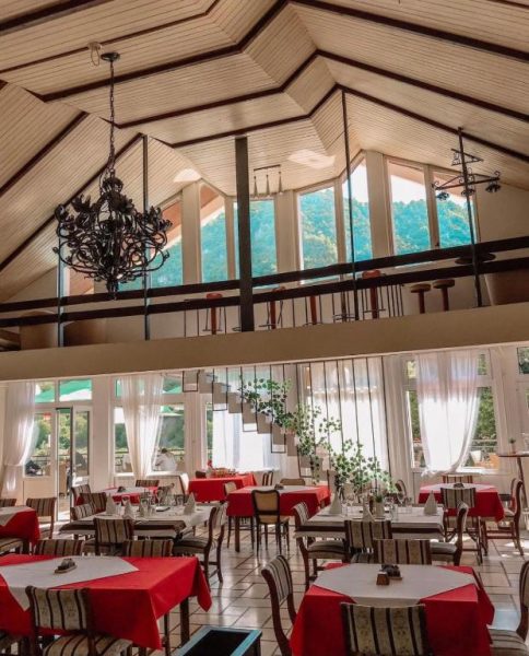 Salón restaurante del Hotel Djokovic con mesas rojas, techo de madera y vistas al bosque