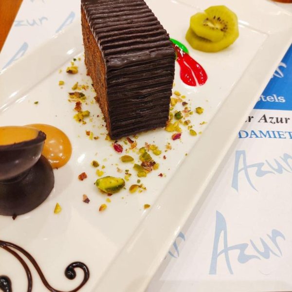 Elegante postre de tarta de chocolate con pistachos y kiwi en el restaurante del Lamar Azur Hotel