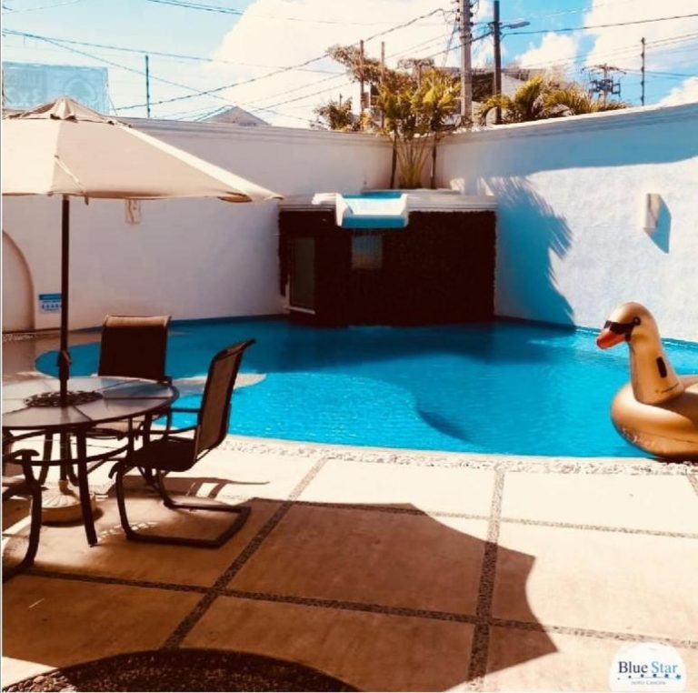 Piscina exterior con flotador cisne y área de descanso con sombrilla en Hotel Blue Star Cancún
