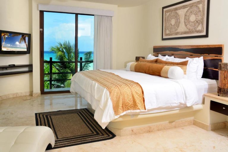 Habitación de lujo con cama king y balcón con vista al mar turquesa en El Taj Oceanfront and Beachside Condo Hotel