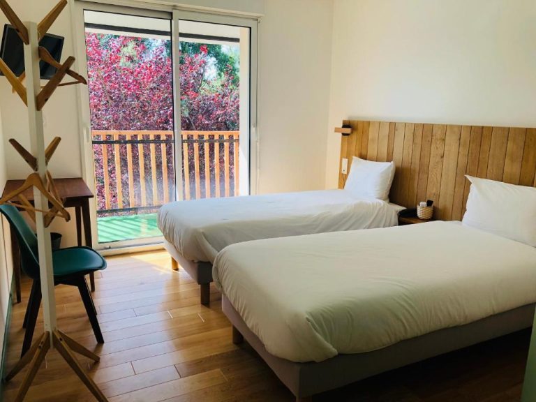 Habitación twin con dos camas y balcón con vistas a jardín en Logis Hôtel Les Tilleuls