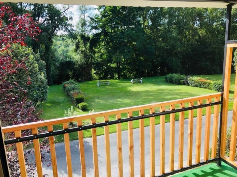 Vista del jardín exterior con césped y bancos desde el balcón de madera del Logis Hôtel Les Tilleuls