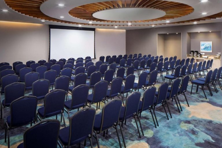 Sala de conferencias con sillas azules y pantalla de proyección en Hyatt Place Aruba Airport