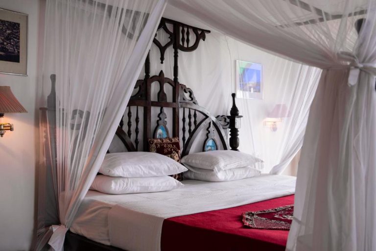 Habitación con cama de dosel tallada en madera y mosquitera blanca en Tembo House Hotel