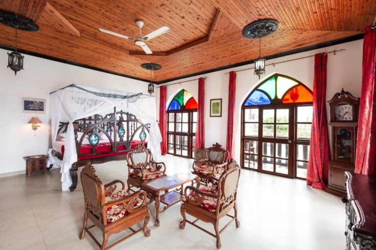 Suite colonial con cama con dosel y ventanas emplomadas de colores en Tembo House Hotel Zanzíbar