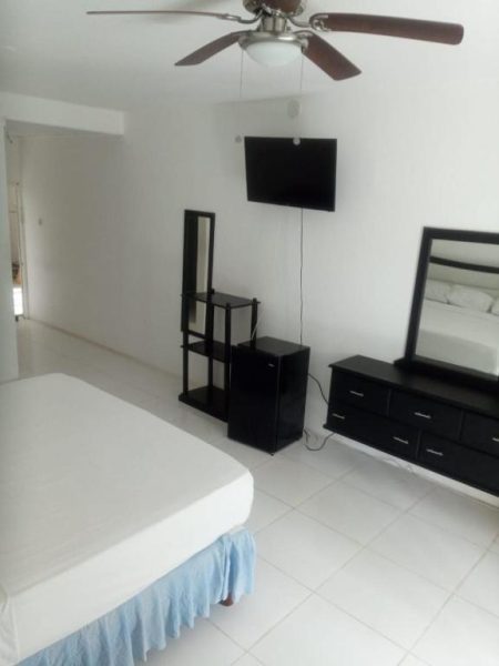 Habitación doble con cama, televisor y ventilador de techo en Negril Beach Club Condos Jamaica