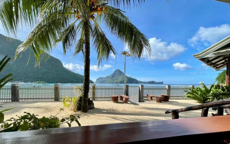 Terraza de arena con palmera y vistas al mar en Chislyk Inn, con montañas al fondo en El Nido