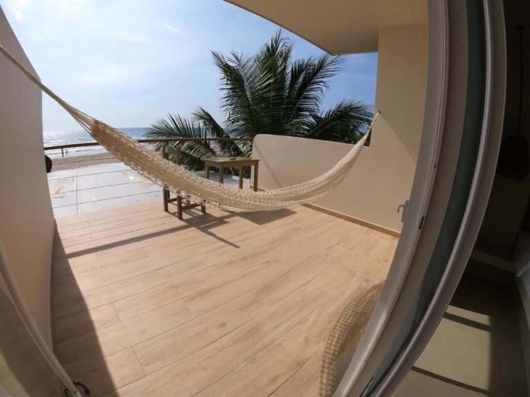 Terraza con hamaca y vista al mar en Hotel Kundalini, con palmeras y suelo de madera
