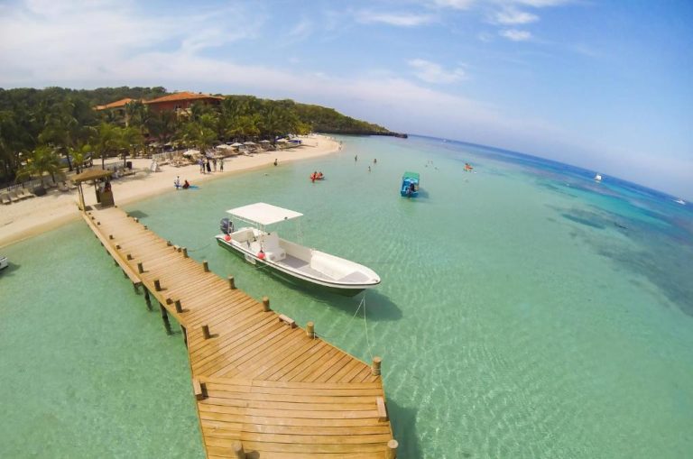 Muelle de madera con lancha amarrada y playa de aguas turquesas en Infinity Bay Spa & Beach Resort