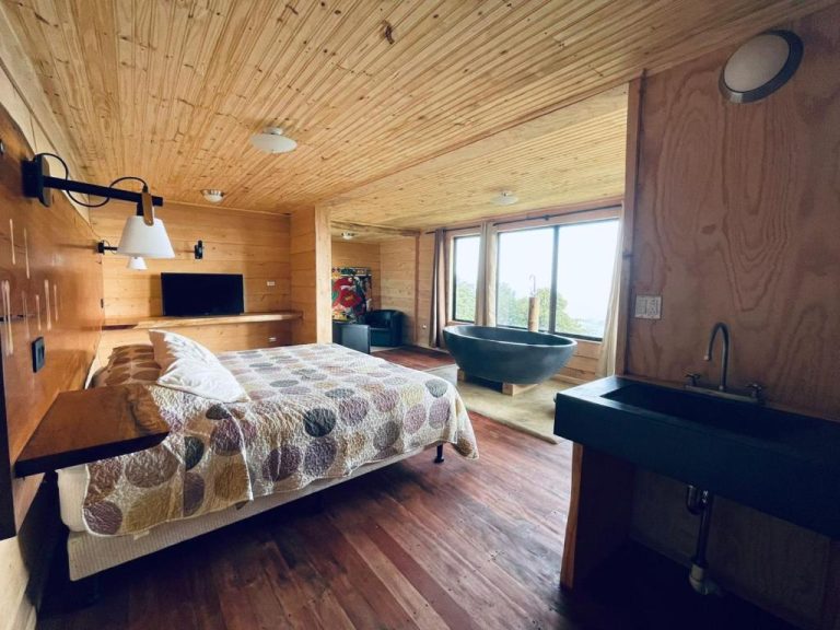 Suite de madera con cama doble, bañera exenta negra y vistas al exterior en Altura Hotel